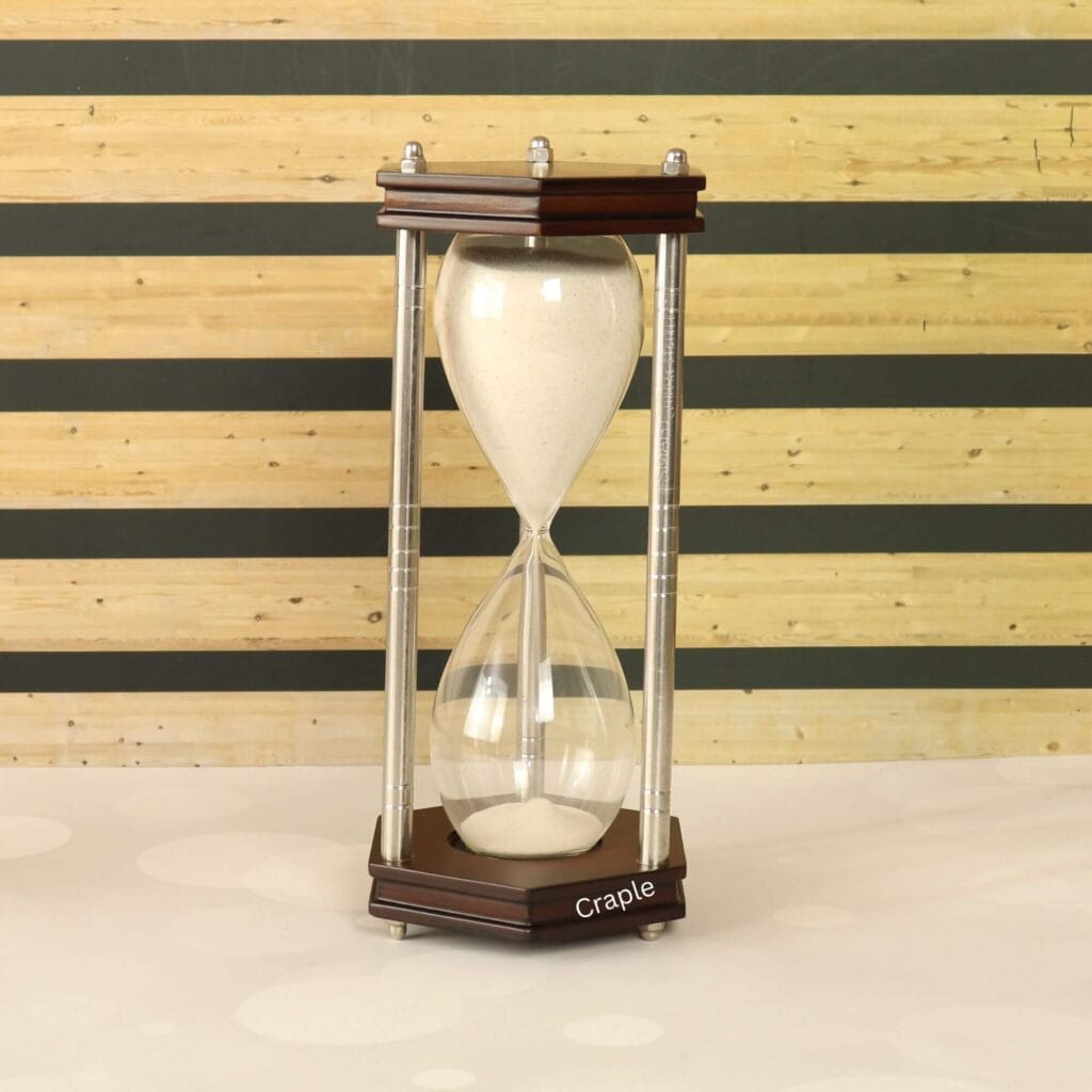 A 30-minute hourglass with white sand, framed by hexagonal dark wood bases and nickel-finished brass pillars.