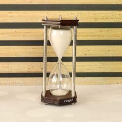 A 30-minute hourglass with white sand, framed by hexagonal dark wood bases and nickel-finished brass pillars.