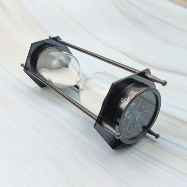 A hexagonal hourglass and compass combination with a black antique finish, shown lying on its side.