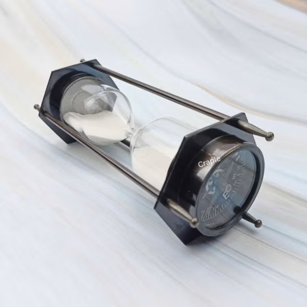 A hexagonal hourglass and compass combination with a black antique finish, shown lying on its side.