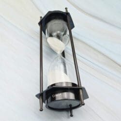 The hexagonal brass sand timer tilted to show the white sand flowing through the hourglass.