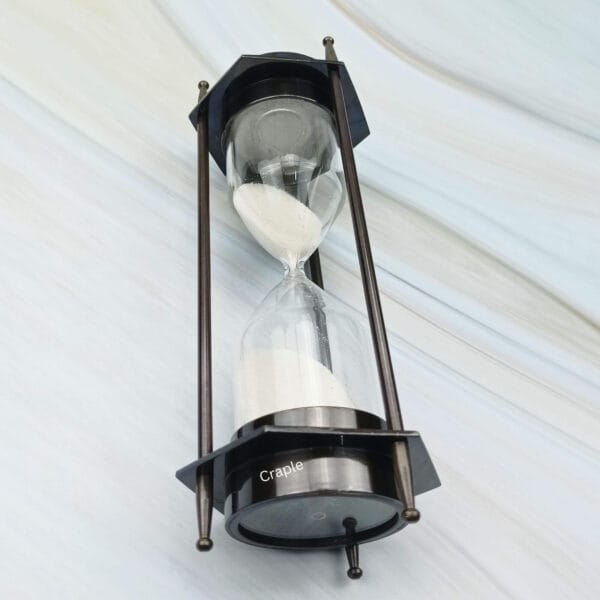 The hexagonal brass sand timer tilted to show the white sand flowing through the hourglass.