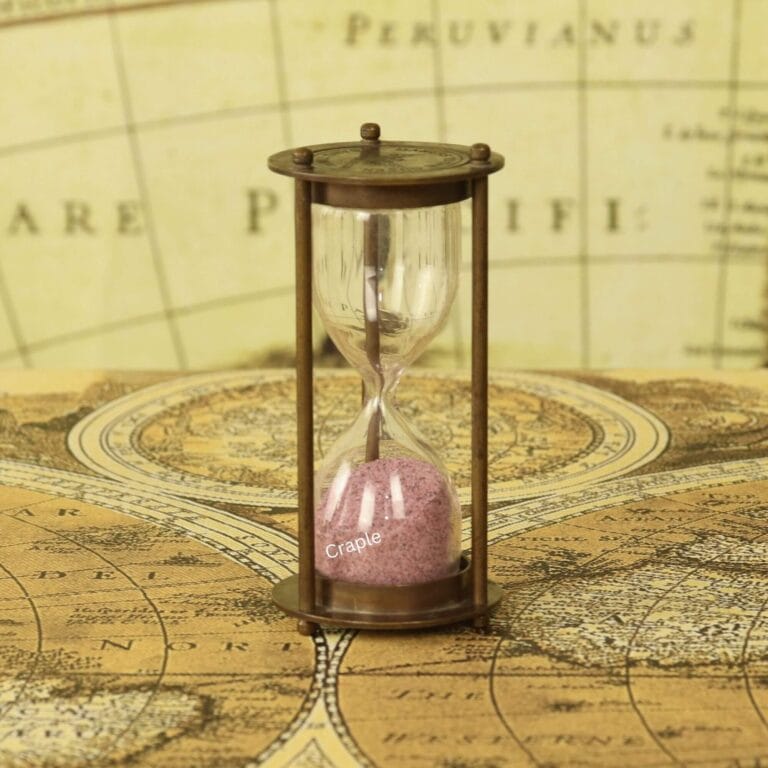 A small antique brass 1-minute hourglass with light pink sand, standing on a vintage world map.