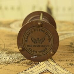 Close-up of the top of the brass hourglass, showing the "Makers to the Queen" engraving.