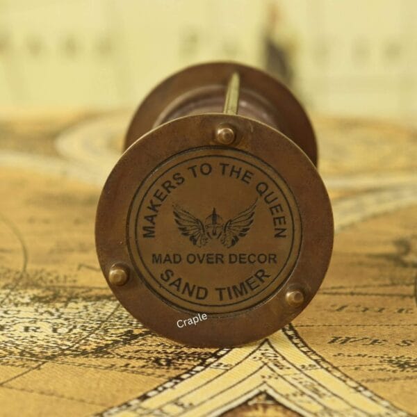 Close-up of the top of the brass hourglass, showing the "Makers to the Queen" engraving.