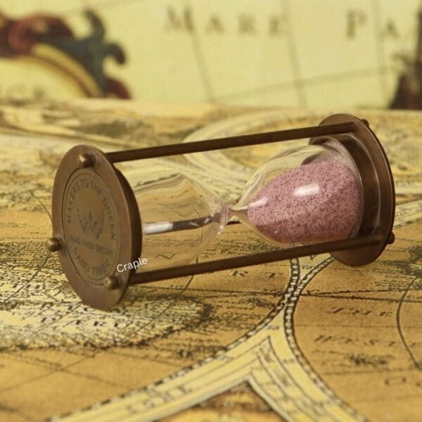 The vintage pink sand hourglass resting on its side, showcasing the antique brass finish and frame.