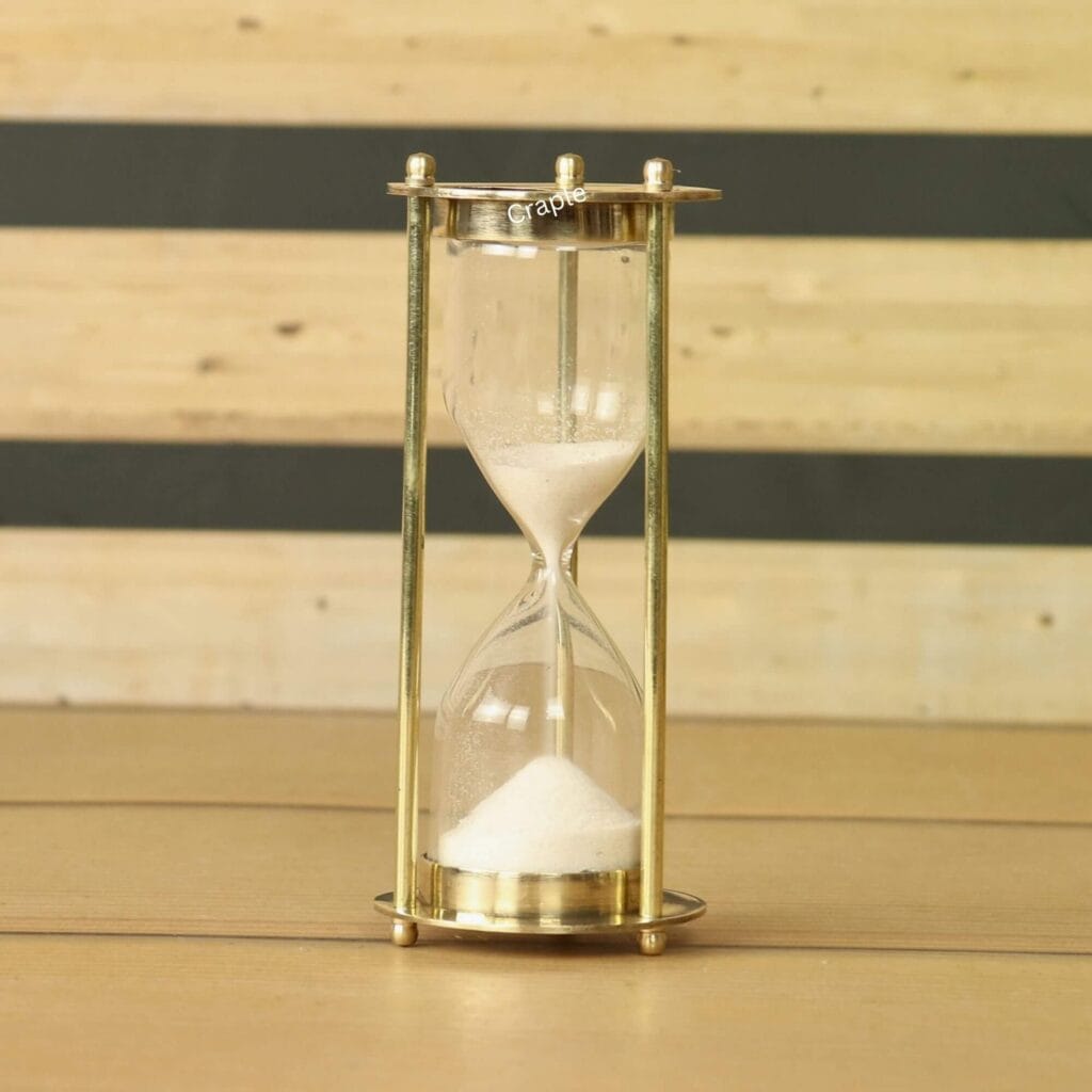 Miniature 1-minute sand timer with a shiny brass frame and fine white sand, standing on a wooden surface.