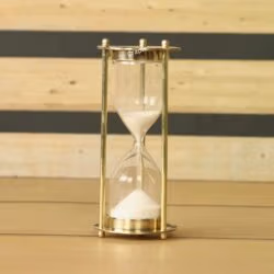 Miniature 1-minute sand timer with a shiny brass frame and fine white sand, standing on a wooden surface.