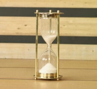Miniature 1-minute sand timer with a shiny brass frame and fine white sand, standing on a wooden surface.