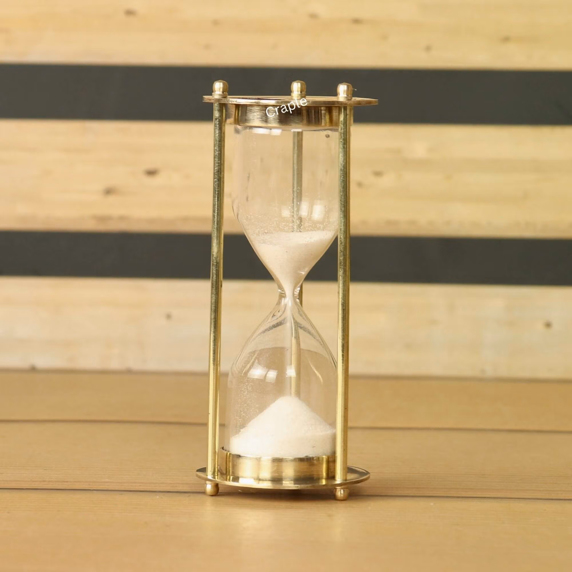 Miniature 1-minute sand timer with a shiny brass frame and fine white sand, standing on a wooden surface.