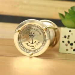 Close-up of the engraved brass top of the sand timer, featuring a 'Marine Arts 1917' nautical anchor logo.