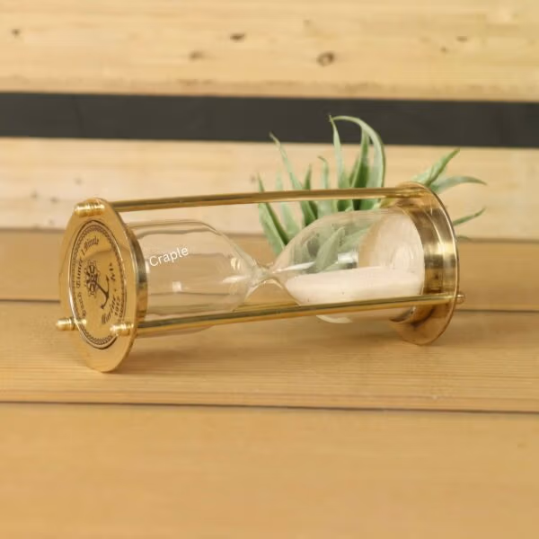 The miniature brass sand timer used as a decorative desktop accessory next to a small succulent plant.