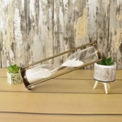 The tall white sand hourglass used as a stylish decorative accessory on a wooden desk next to a plant.