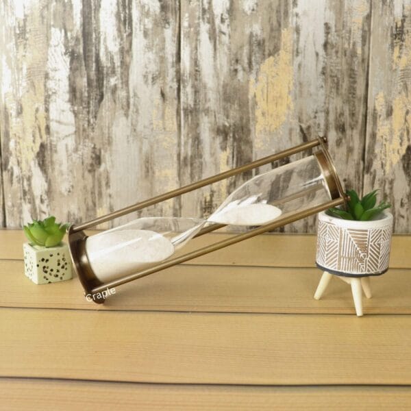 The tall white sand hourglass used as a stylish decorative accessory on a wooden desk next to a plant.