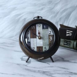 An antique wooden desk clock with a unique patchwork dial, a brown antique finish, and a classic round shape.