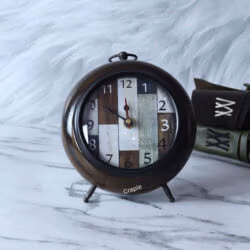 An antique wooden desk clock with a unique patchwork dial, a brown antique finish, and a classic round shape.
