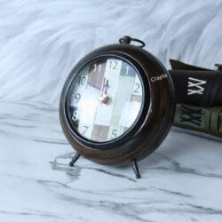 Angled view of the rustic patchwork desk clock, showing its round wooden body and sturdy metal legs.