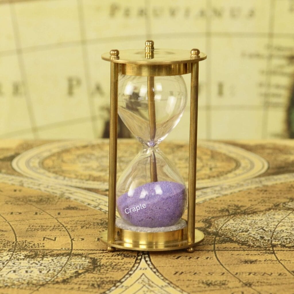 A petite 1-minute hourglass with a shiny brass frame and purple sand, displayed on a vintage map.