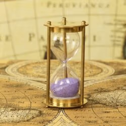 A petite 1-minute hourglass with a shiny brass frame and purple sand, displayed on a vintage map.