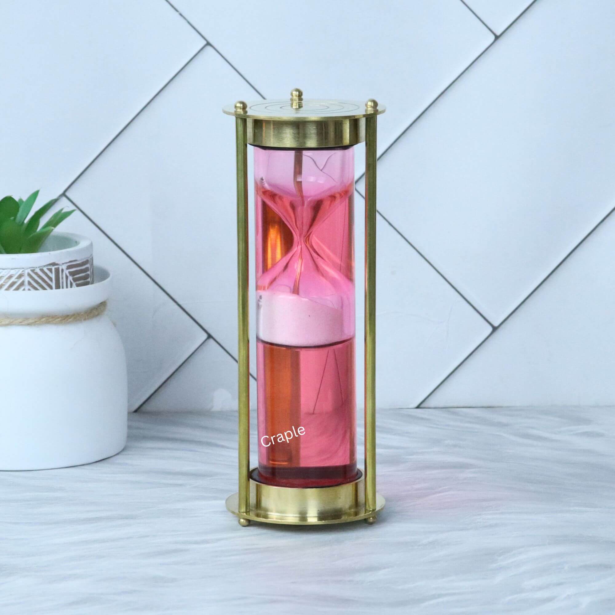 Pink Liquid Floating Hourglass-1 An elegant pink liquid floating hourglass with a shiny brass frame, showing the internal sand timer.