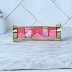 The decorative pink liquid hourglass lying horizontally, showcasing the floating sand timer within its brass frame.