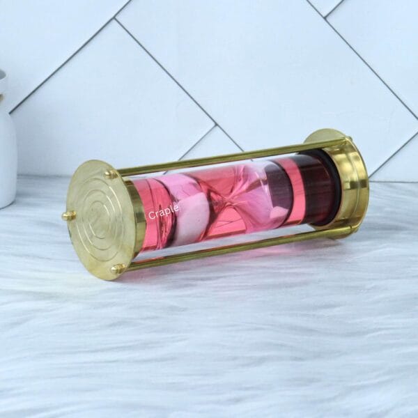 End view of the floating hourglass, showing the polished brass end cap and the pink liquid-filled glass tube.