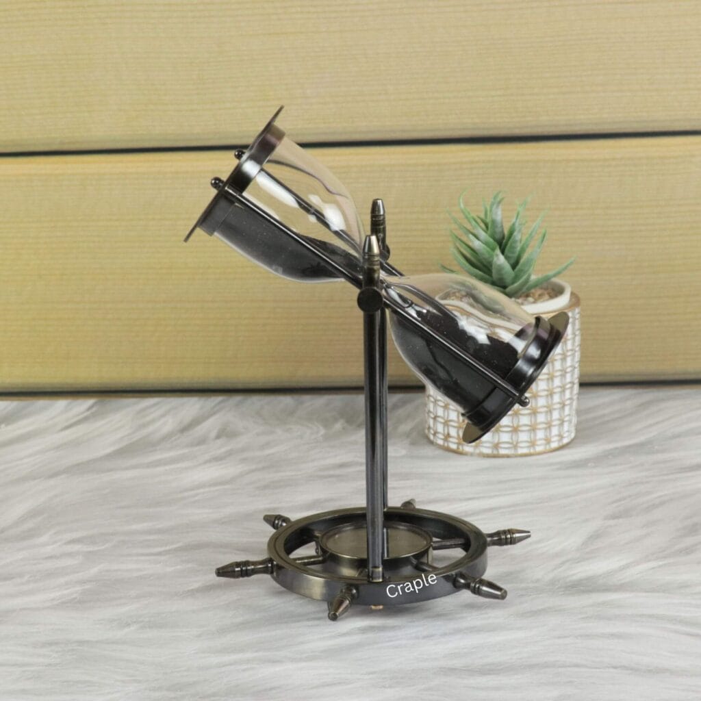 The nautical sand timer swiveling within its black antique brass frame, with black sand flowing through the glass.