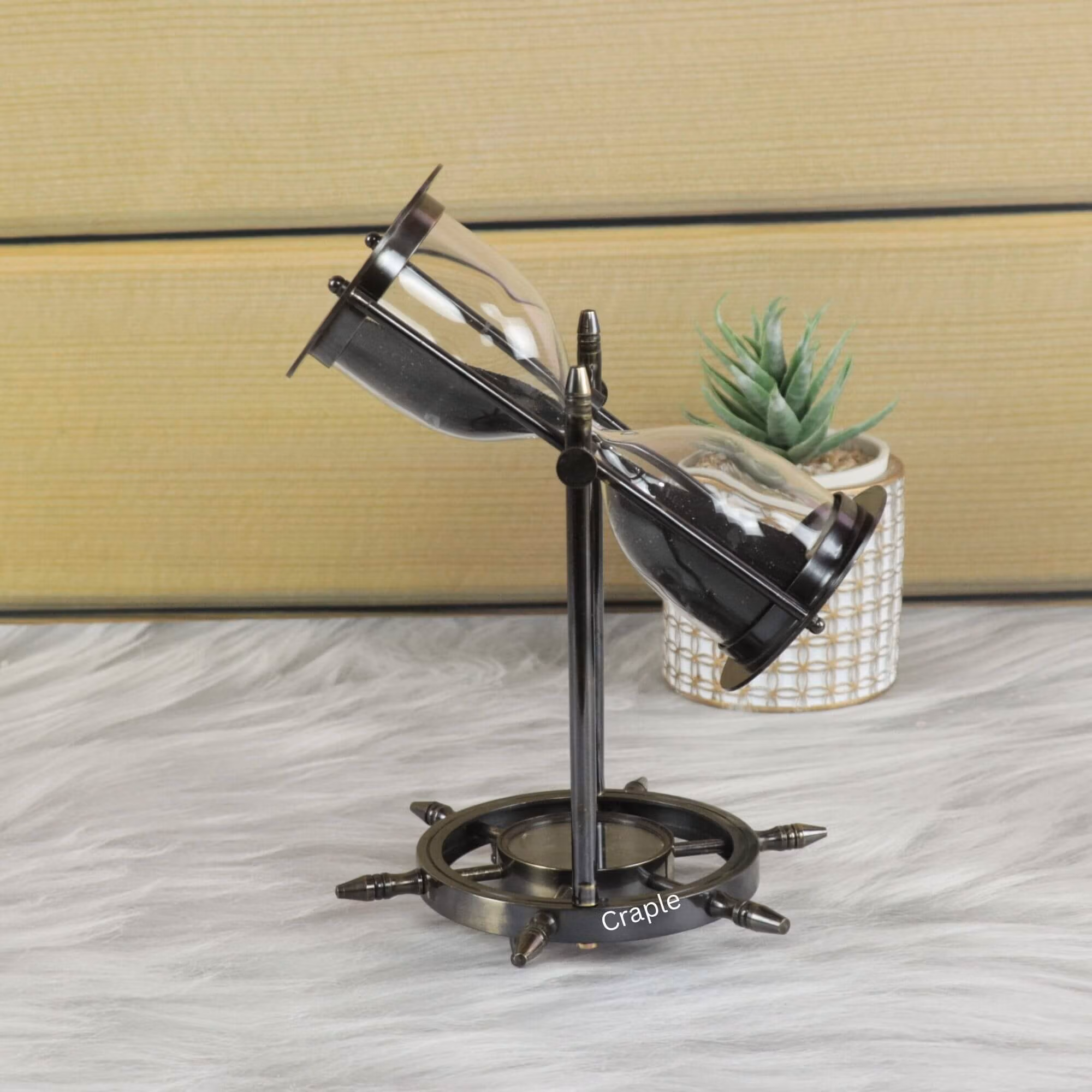 The nautical sand timer swiveling within its black antique brass frame, with black sand flowing through the glass.