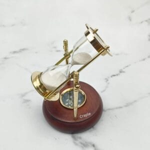 Rotating brass hourglass with white sand and a built-in compass, mounted on a round, polished wooden base.
