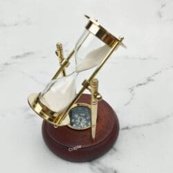 The brass sand timer tilted to the side, showcasing the swiveling mechanism and the compass in the wooden base.