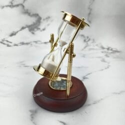 The 2-minute sand timer tilted on its axis, showing the white sand and the brass frame detail.
