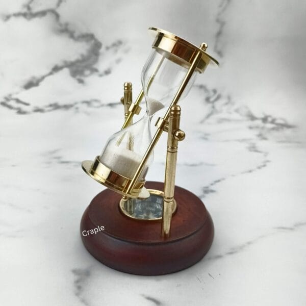 The 2-minute sand timer tilted on its axis, showing the white sand and the brass frame detail.