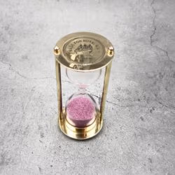Top-down view of a Royal Navy brass sand timer with pink sand, showing the engraved top plate.
