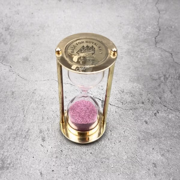 Top-down view of a Royal Navy brass sand timer with pink sand, showing the engraved top plate.