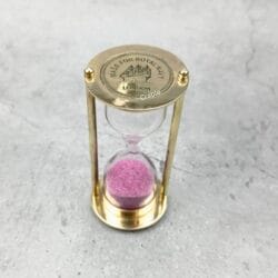 Front view of the 3-minute brass hourglass, featuring bright pink sand and a polished finish.