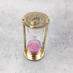 Front view of the 3-minute brass hourglass, featuring bright pink sand and a polished finish.
