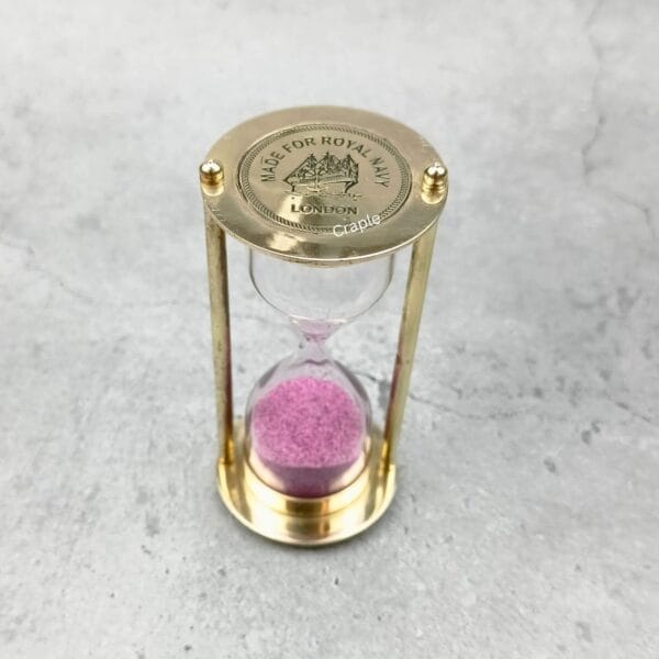 Front view of the 3-minute brass hourglass, featuring bright pink sand and a polished finish.