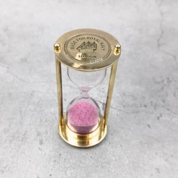 Front view of the 3-minute brass hourglass, featuring bright pink sand and a polished finish.