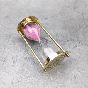 A 3-minute Royal Navy hourglass with a polished brass frame and pink sand, resting on its side to showcase its design.