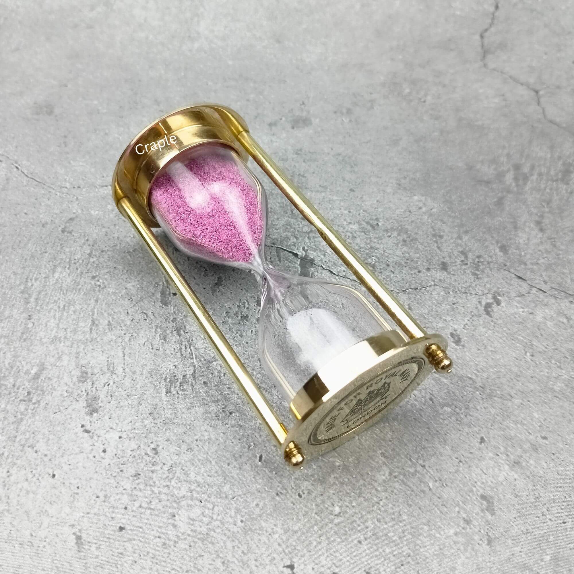 Royal Navy 3-Minute Sand Timer-5 A 3-minute Royal Navy hourglass with a polished brass frame and pink sand, resting on its side to showcase its design.