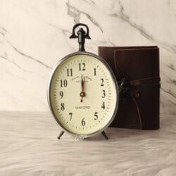 A vintage-style silver aluminum desk clock with a hanging loop, featuring an off-white dial and classic Arabic numerals.