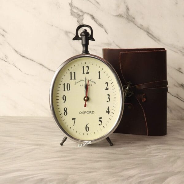 A vintage-style silver aluminum desk clock with a hanging loop, featuring an off-white dial and classic Arabic numerals.