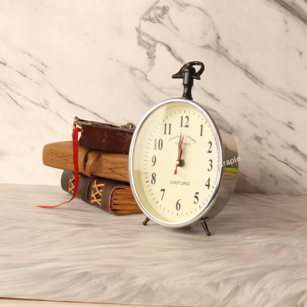 The silver aluminum pocket-watch-style clock displayed as a decorative piece next to a stack of vintage books.