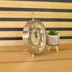 Angled view of the silver skeleton table clock, showcasing its polished nickel finish next to a small plant.