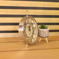 Angled view of the silver skeleton table clock, showcasing its polished nickel finish next to a small plant.