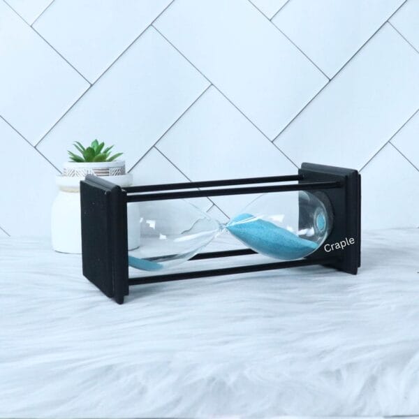 The 30-minute black sand timer resting horizontally, showcasing its rectangular frame and glass bulb.