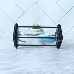 The modern blue sand hourglass displayed as a decorative piece on a white surface next to a plant.