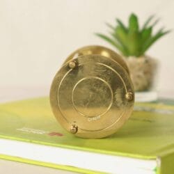 Close-up of the polished brass base of the decorative hourglass sand timer, resting on a book.