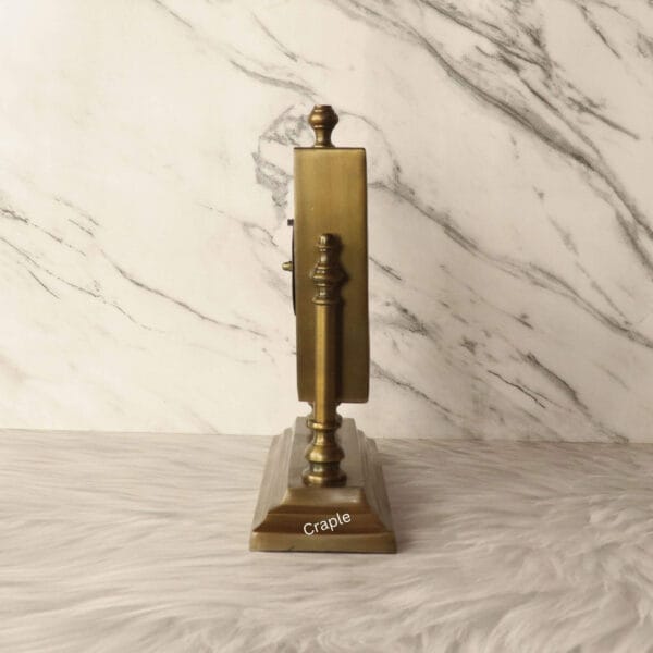 Side profile of the antique brass table clock, highlighting its slim frame and ornate support posts.