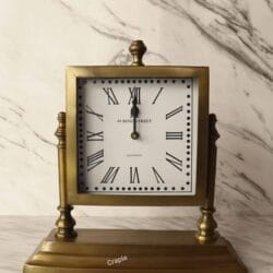 Close-up of the vintage-style clock face with Roman numerals and the heavy, decorative antique brass base.